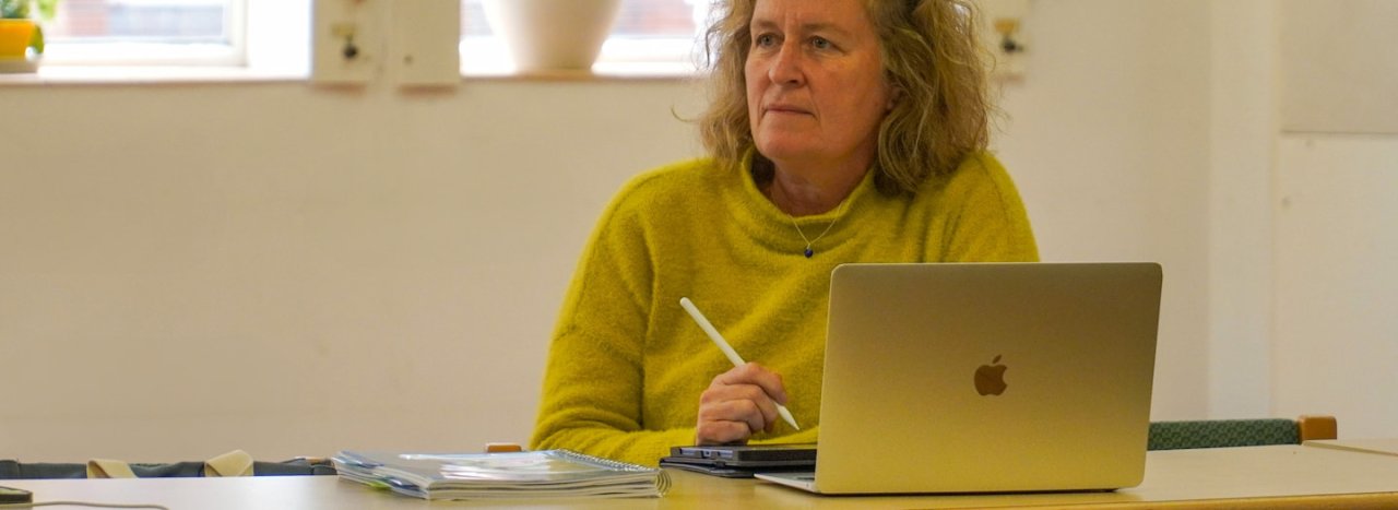 A student dressed in a yellow jumper and with a laptop in front of her, listening to a lesson, as part of All Nations' postgraduate courses.