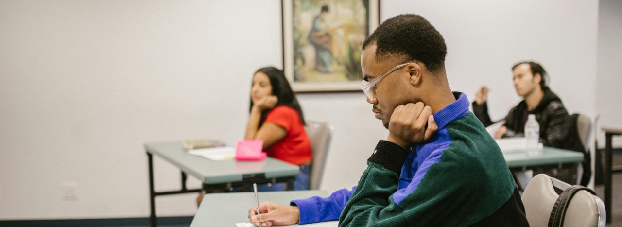 A male student in a classroom taking notes with a further female and male student in the background, representing the shorter certificate course at All Nations.