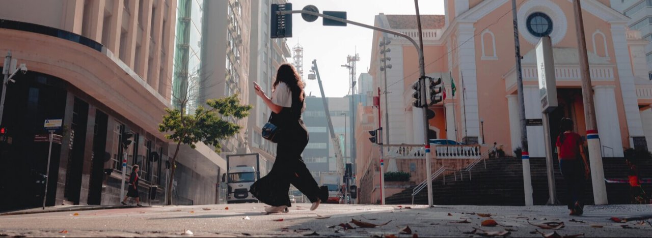 A woman crossing an empty road near a pink and white church to the right, representing mission and church courses.