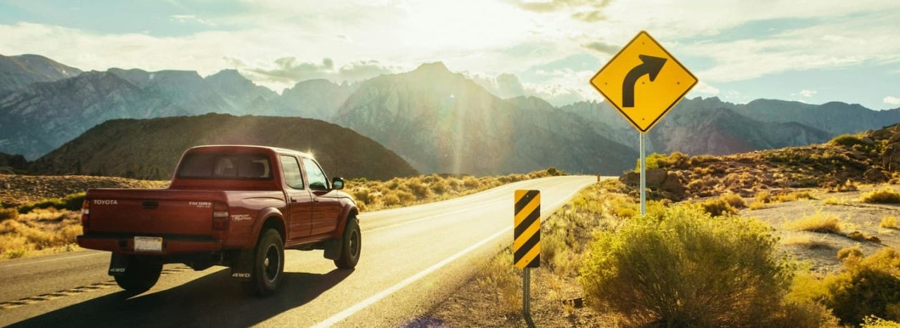 A red pick-up truck on a route in the mountains with traffic signs to the right, representing All Nations En route course.