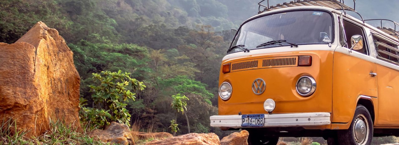 A VW campervan in mustard yellow in a remote setting with some foliage to the right representing the Encounter course for All Nations college.