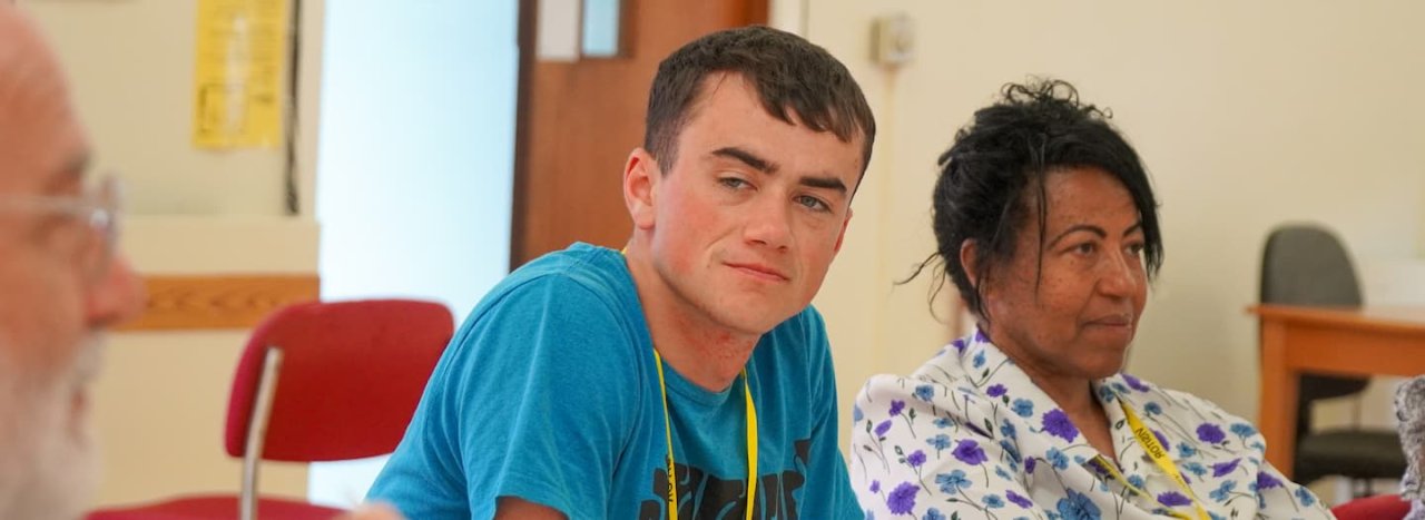 An engaged student dressed in blue, alongside another student looking away, listening to a teacher, representing the Community Transformation: Principles & Practices course at All Nations.