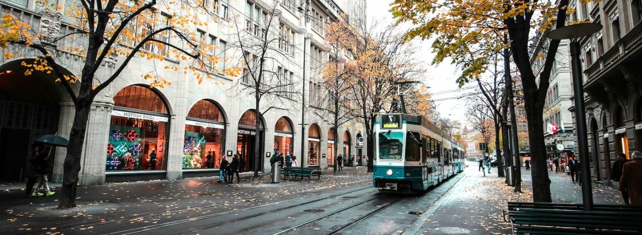 Green tram in an elegant European boulevard, with shops flanking both sides of it, representing All Nations' course in Mission in Europe: Context and Practice.