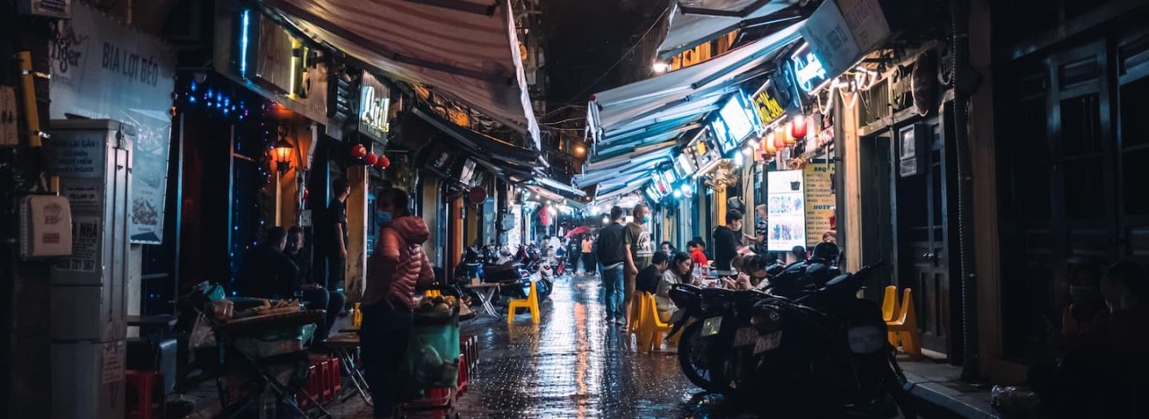 A night scene in Asia with various illuminated stores, people and motorcycles in the foreground, representing our Missiology courses.