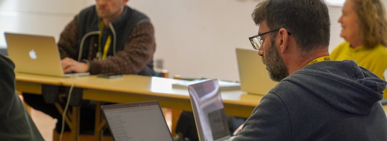 An older student wearing a hoodie and glasses looking at his laptop computer, representing undergraduate degree courses at All Nations college.
