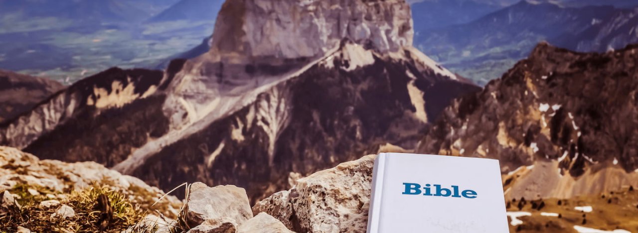 A copy of a white Bible placed on a rock looking out over a view of mountains, representing the course in Missiology at All Nations.