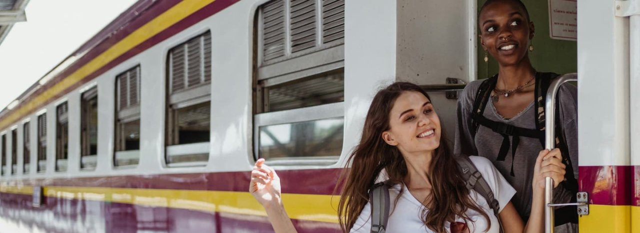Two young women about to board a train, holding on to the handle, possibly abroad, representing All Nations Express course.