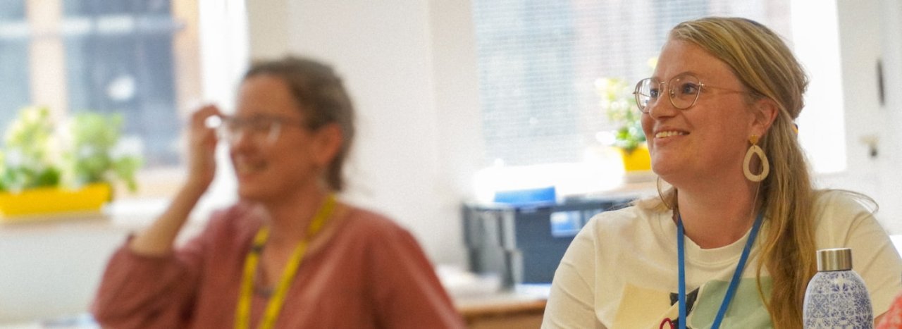 A female student smiling and happy in the foreground to the right and an out of focus student to the left, representing Other courses run by All Nations.