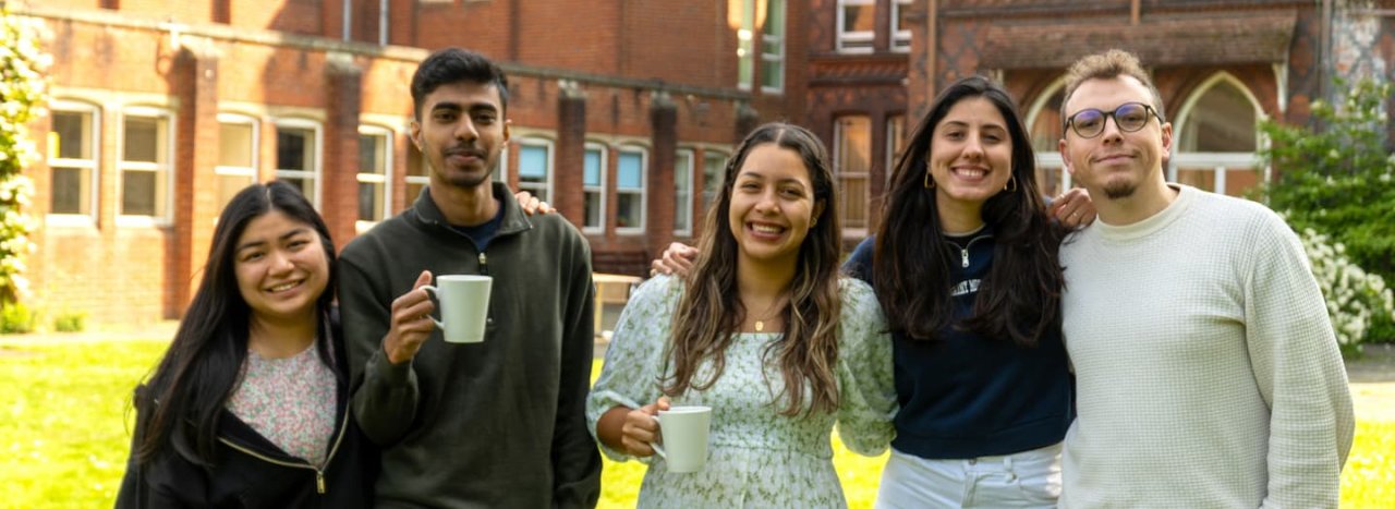 A group of 5 young students, some holding a mug with a drink, standing together as friends, representing open days at All Nations.